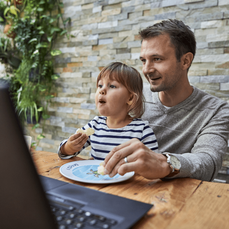 Man and child sitting and eating at a laptop